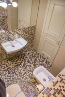 Un baño con lavamanos blanco, inodoro y bañera. El suelo presenta un diseño de mosaicos.