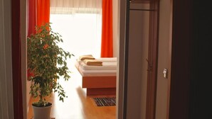 A hallway leading to a bedroom with a bed, a potted plant, and a wooden door. - Garni Hotel Villa Tamara (Moravske Toplice)