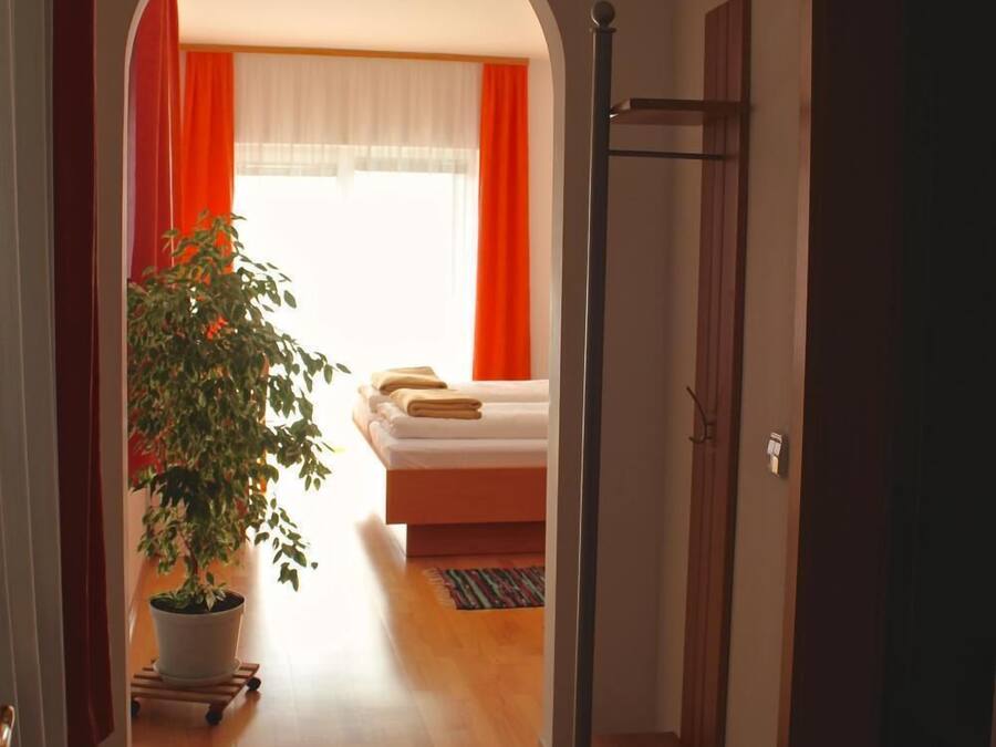 Un pasillo que conduce a un dormitorio con una cama, una planta en maceta y una puerta de madera.