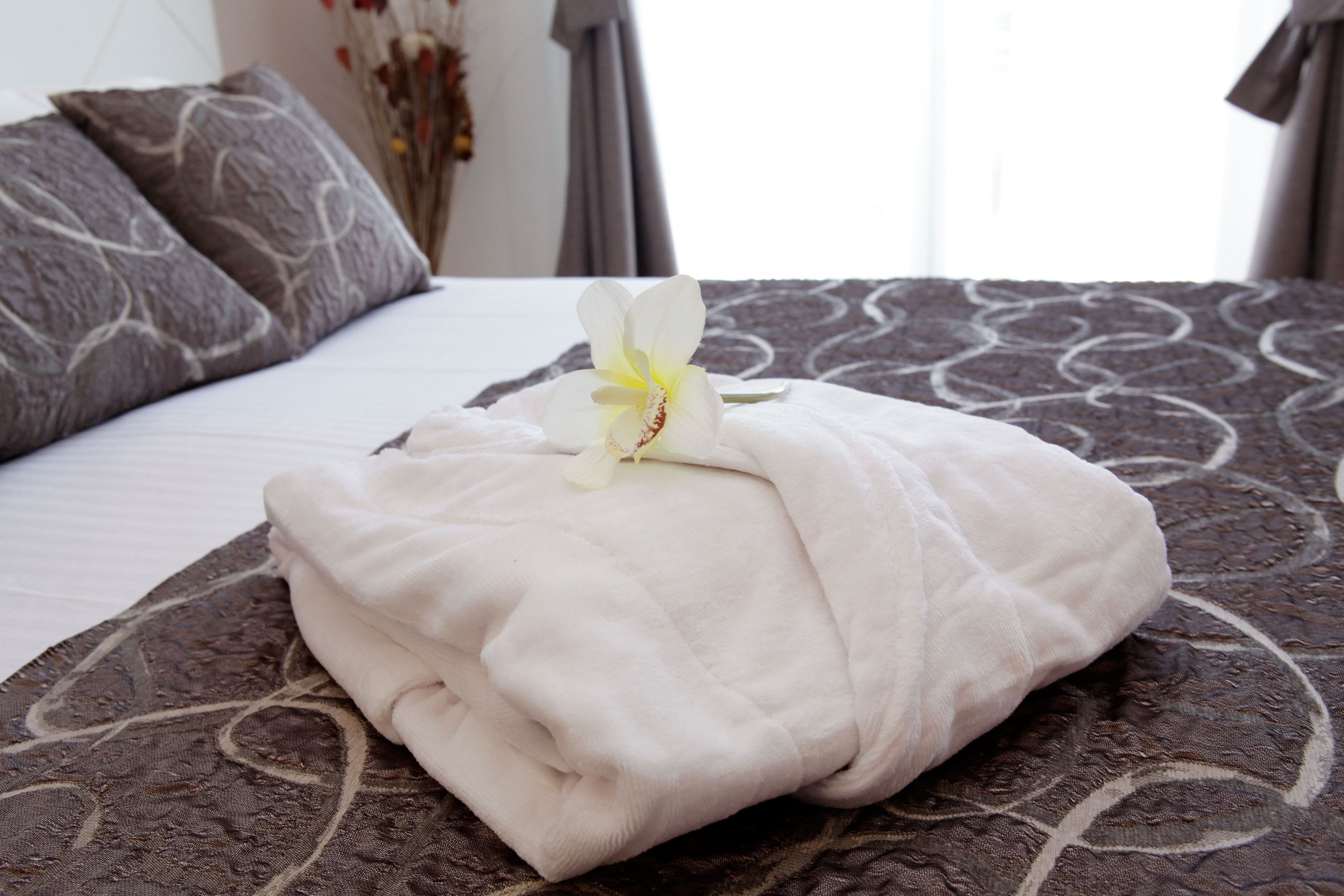 A neatly made bed with a white blanket and a single white flower.