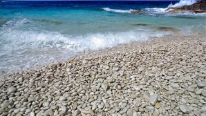 Una playa de guijarros con agua turquesa cristalina y olas rompiendo en la orilla.