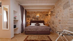 Un dormitorio con pared de piedra, cama con colcha estampada, mesita de noche con lámpara y silla de madera.