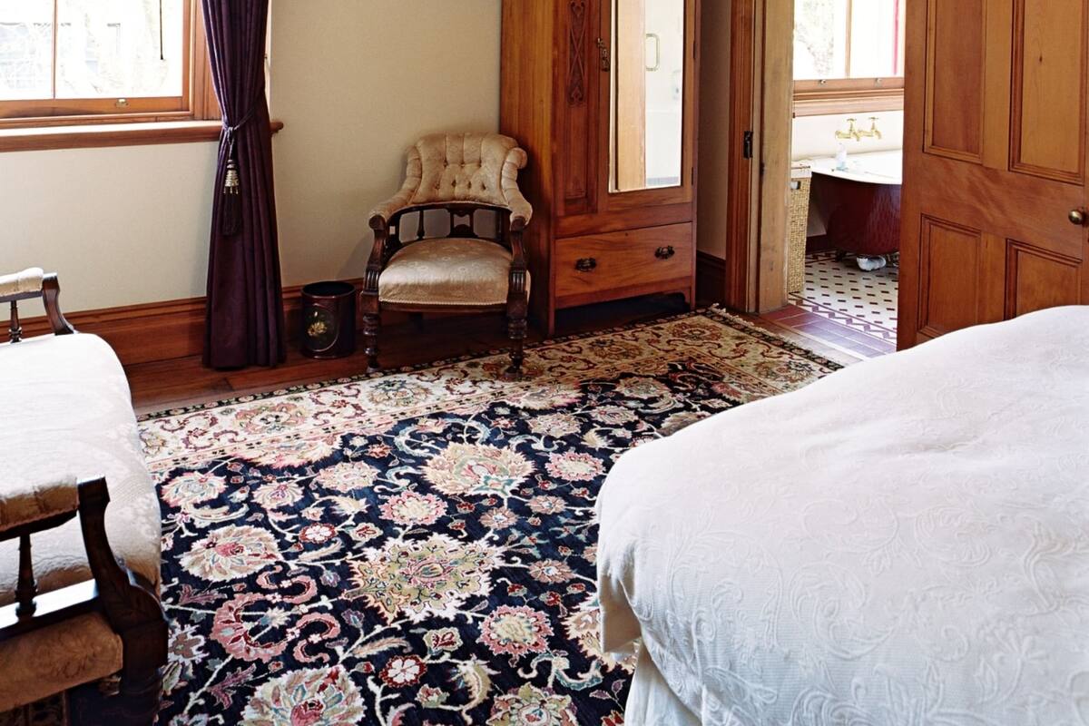 A traditional room with a large wooden wardrobe, a chair, a bed, and a patterned rug.