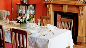 A dining room with a red wall, a chandelier, a fireplace, and a mirror. - Braemar on Parliament Street (Auckland)