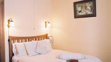 A neatly made bed with a wooden headboard, two wall-mounted lamps, a framed picture, and a patterned rug.