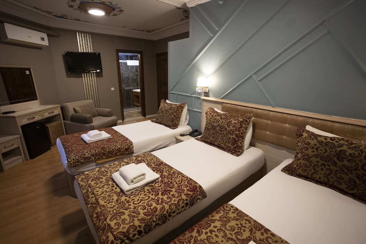 A hotel room with two beds, a desk, a chair, a TV, and a bathroom visible through a glass door.