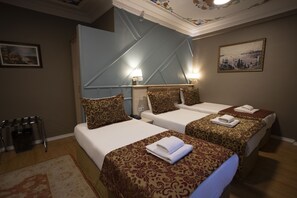 A hotel room with two beds, each with a patterned bedspread and pillows, a small table with a lamp, and a painting on the wall. - Tashkonak Studio Suites (Istanbul)