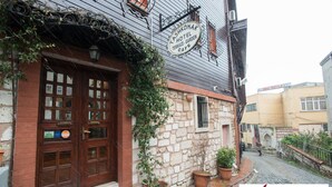 Un edificio tradizionale con una porta di legno, un cartello per il Tashkonak Hotel Terrace Garden Cafe e piante in vaso sui gradini.