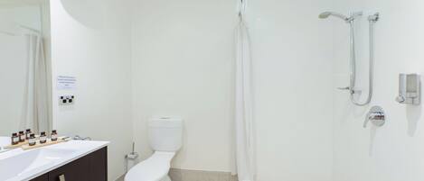 A modern bathroom with a white toilet, a shower with a handheld showerhead, and a vanity with a mirror and a soap dispenser.