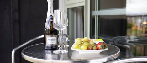 Une bouteille de vin et un verre sur une table en métal, avec une assiette de raisins et une fraise.