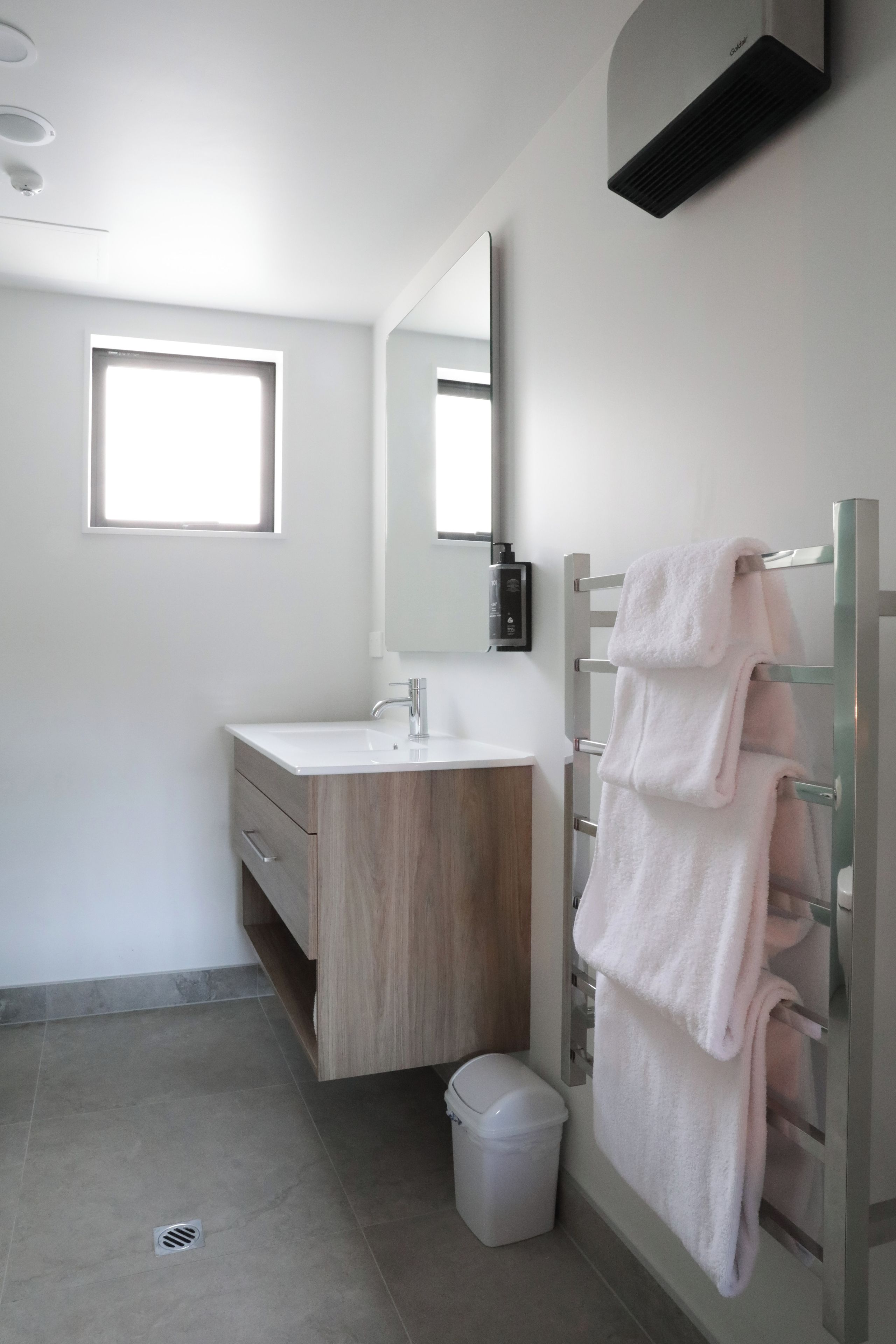 A modern bathroom with a white sink, a mirror, a towel rack, and a shower area.
