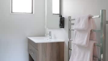 A modern bathroom with a white sink, a mirror, a towel rack, and a shower area.