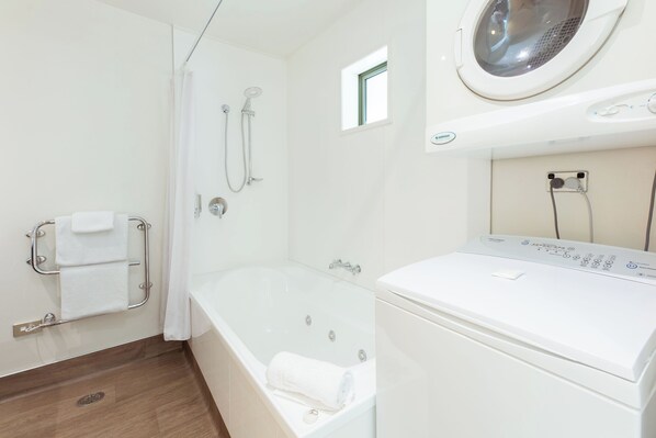 A bathroom with a bathtub, a shower, and a front-loading washing machine. - Clearbrook Motels Wanaka (Wanaka)