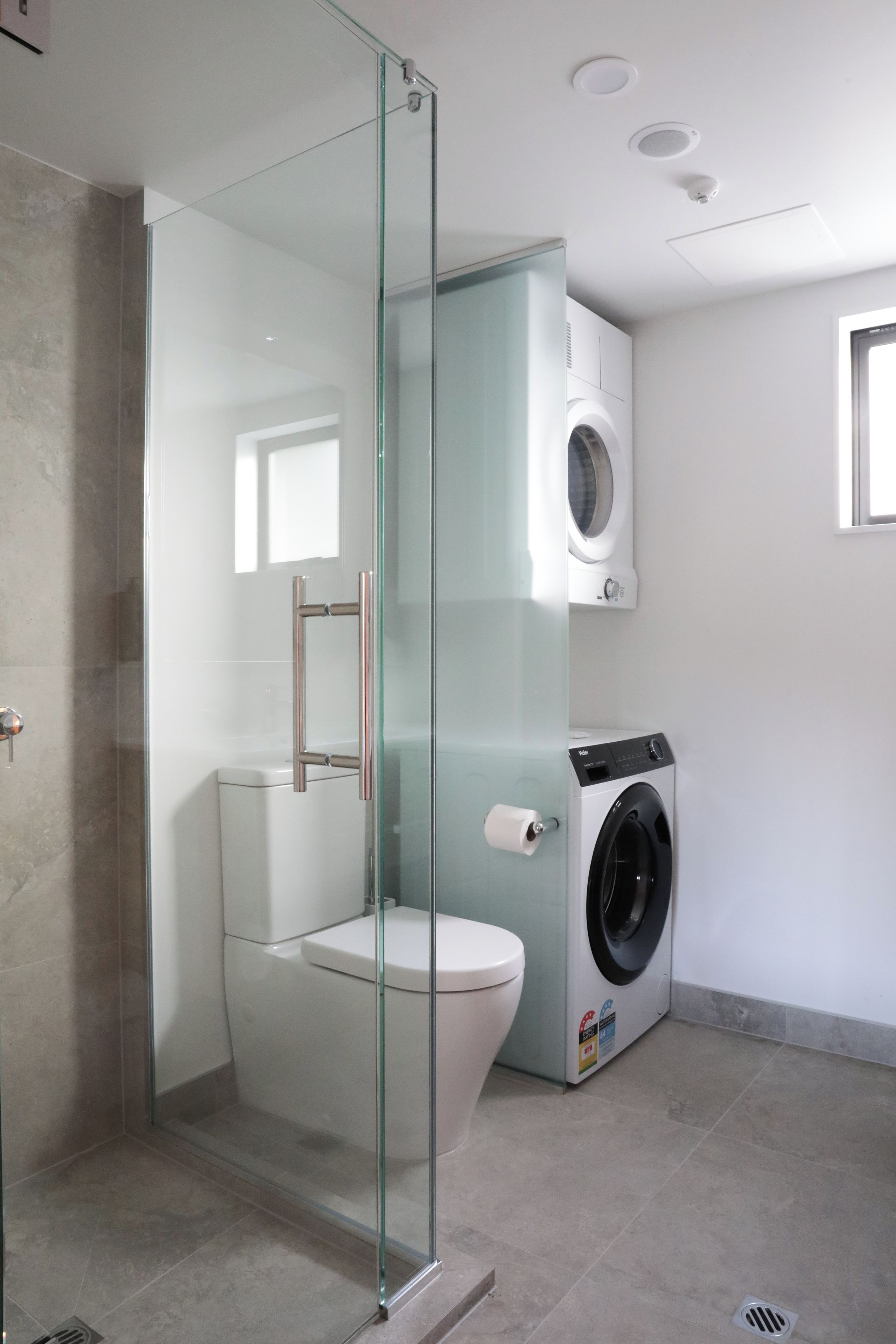 A modern bathroom with a glass-enclosed shower, a toilet, and a washing machine.