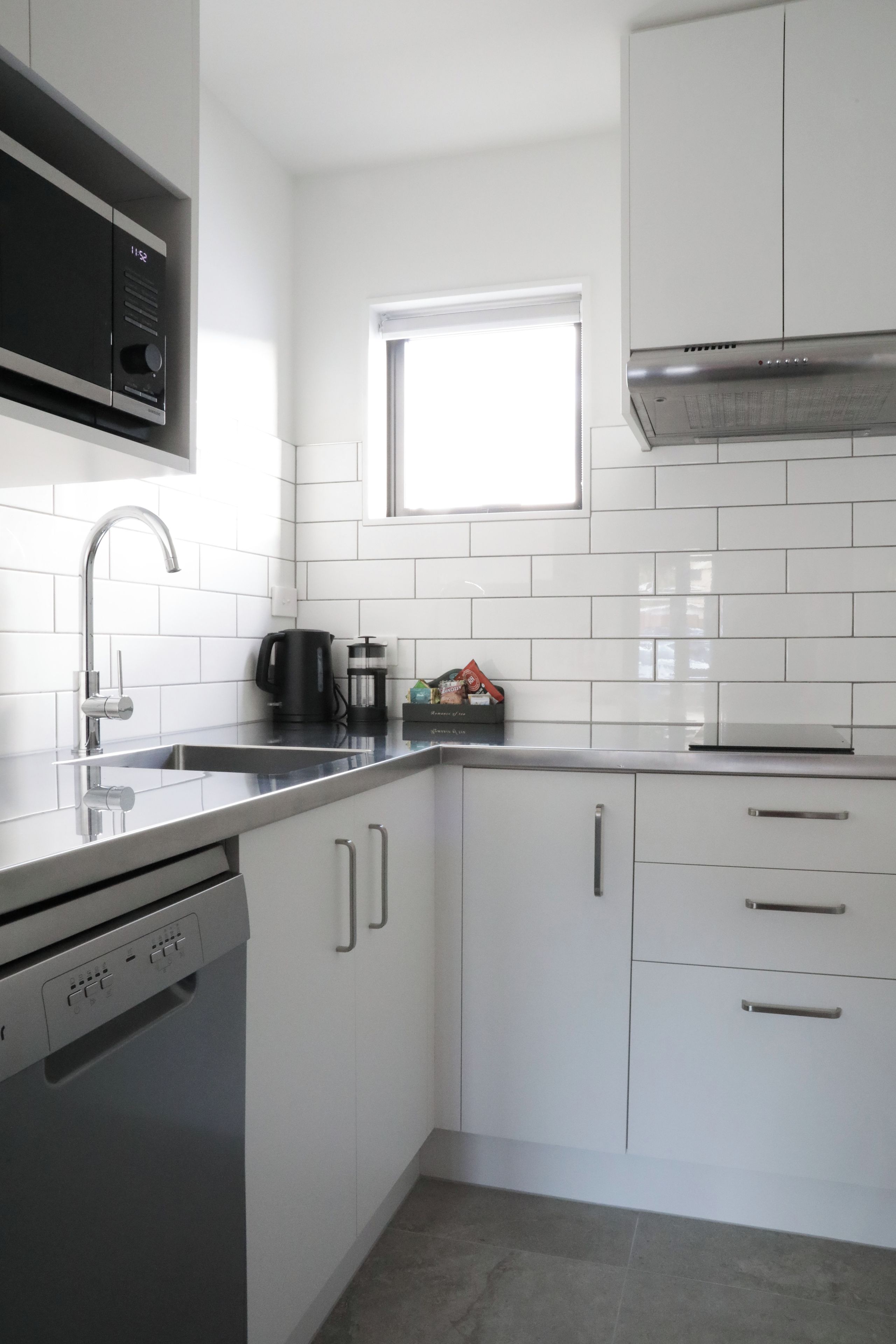 A modern kitchen with white cabinets, stainless steel appliances, and a window above the sink.