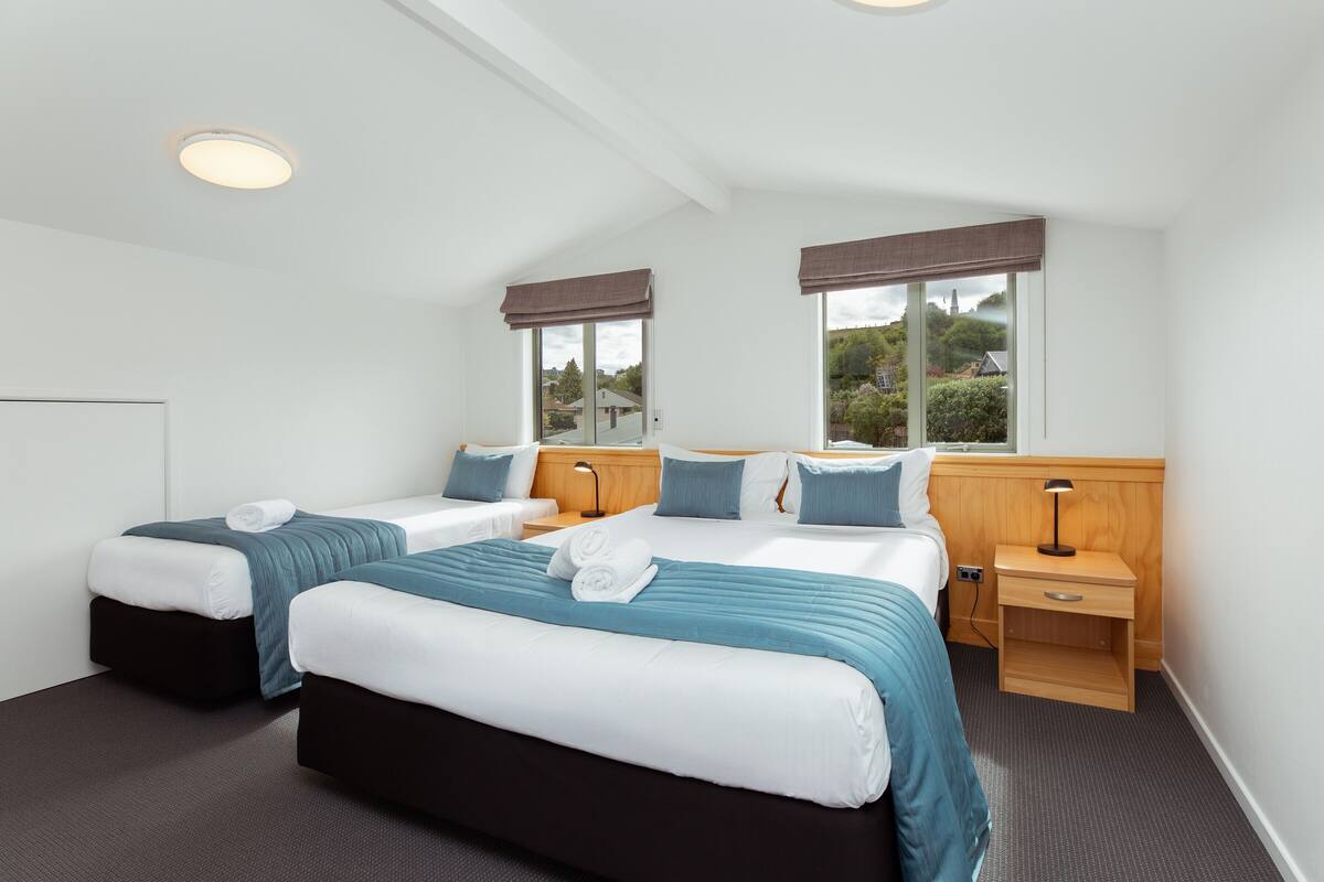 A hotel room with two beds, a nightstand, a window with a view, and a ceiling light.