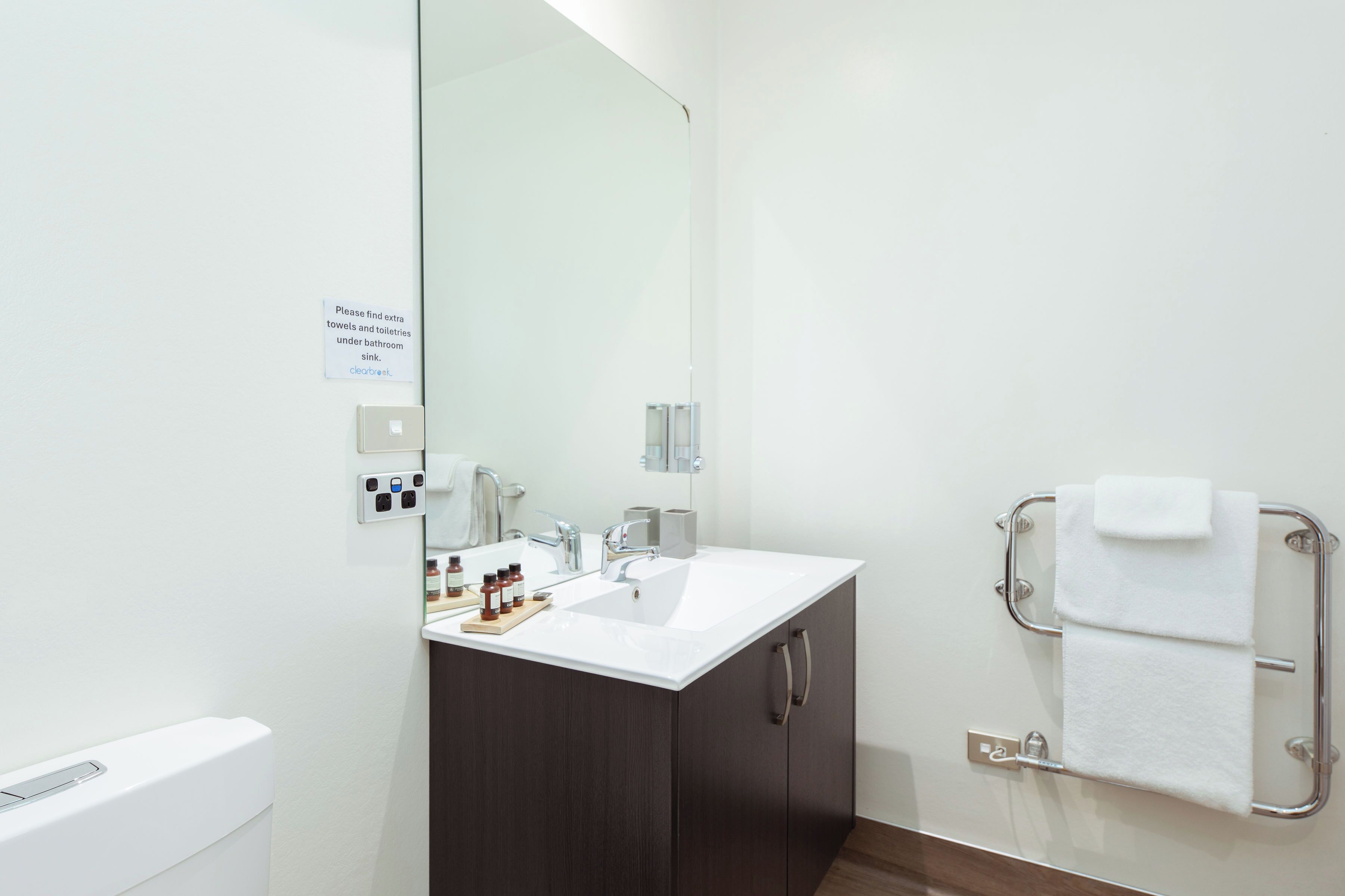 A modern bathroom with a white sink, dark wooden cabinets, a mirror, and a towel rack.