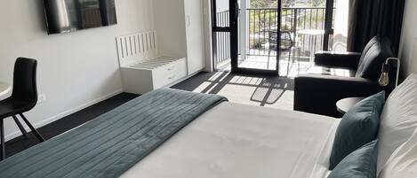 A modern hotel room with a bed, a desk, a chair, a TV, and a balcony with a view of the city.