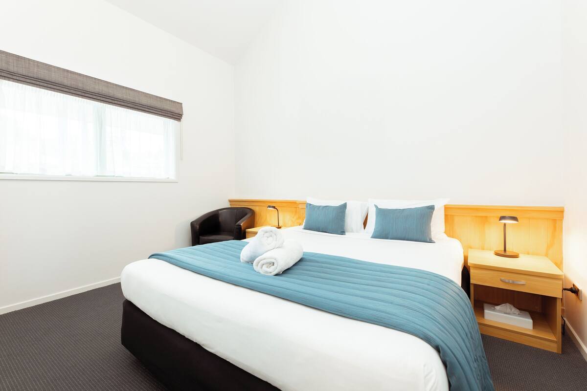 A hotel room with a bed, a nightstand, a chair, and a window with curtains.