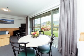 A modern room with a round table, chairs, a TV, and a window with curtains. - Clearbrook Motels Wanaka (Wanaka)