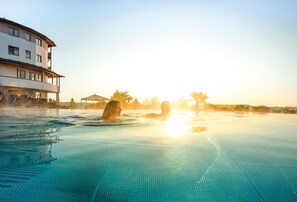 A swimming pool with clear water, surrounded by a building with multiple balconies. - Hotel & Spa Larimar (Stegersbach)