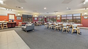Una amplia sala de conferencias con varias mesas y sillas, ventanas grandes con vistas, y un sofá gris.
