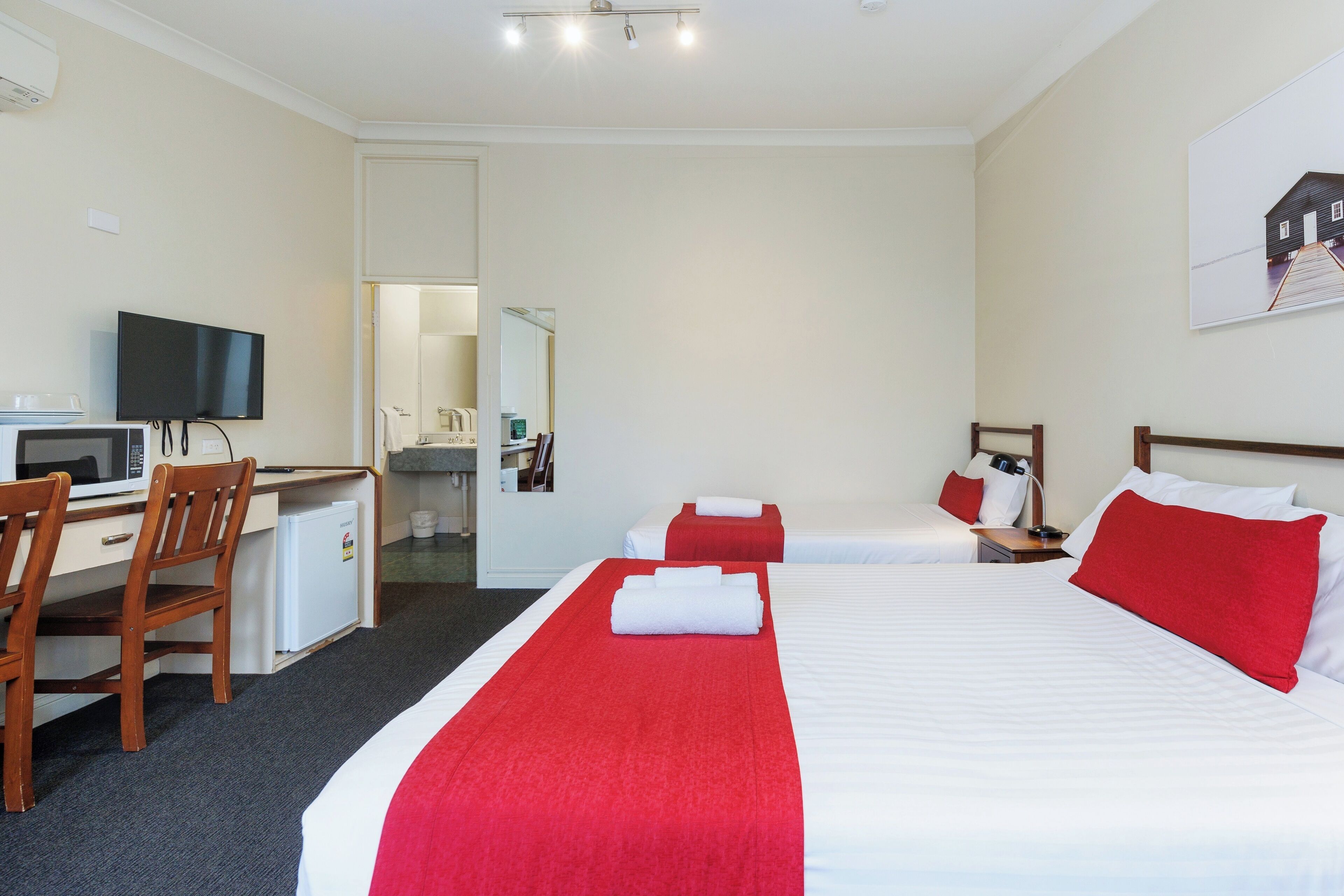 A hotel room with a bed, a desk with a TV, a microwave, and a small refrigerator.