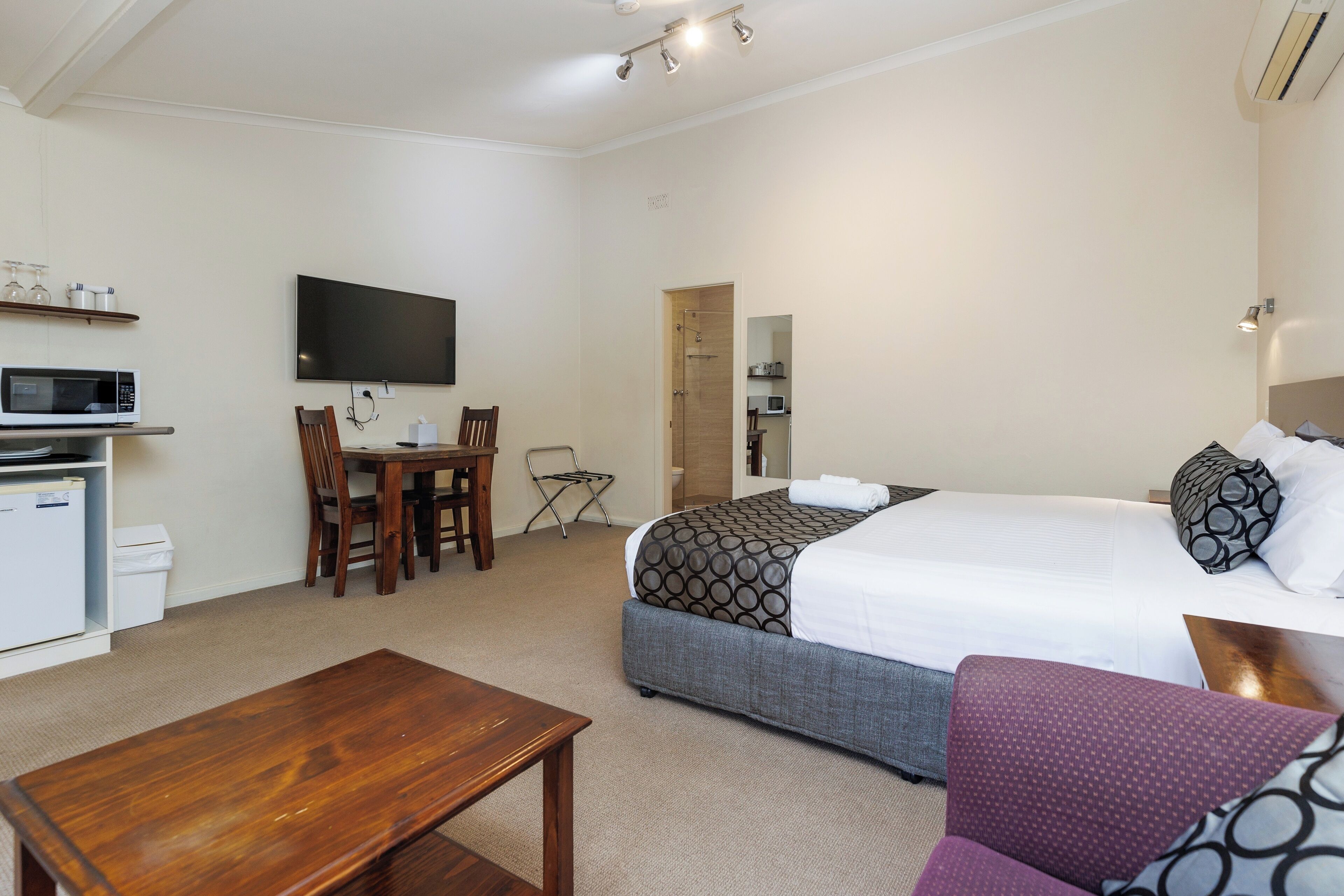 A hotel room with a bed, a desk, a chair, a TV, a microwave, and a small kitchenette.