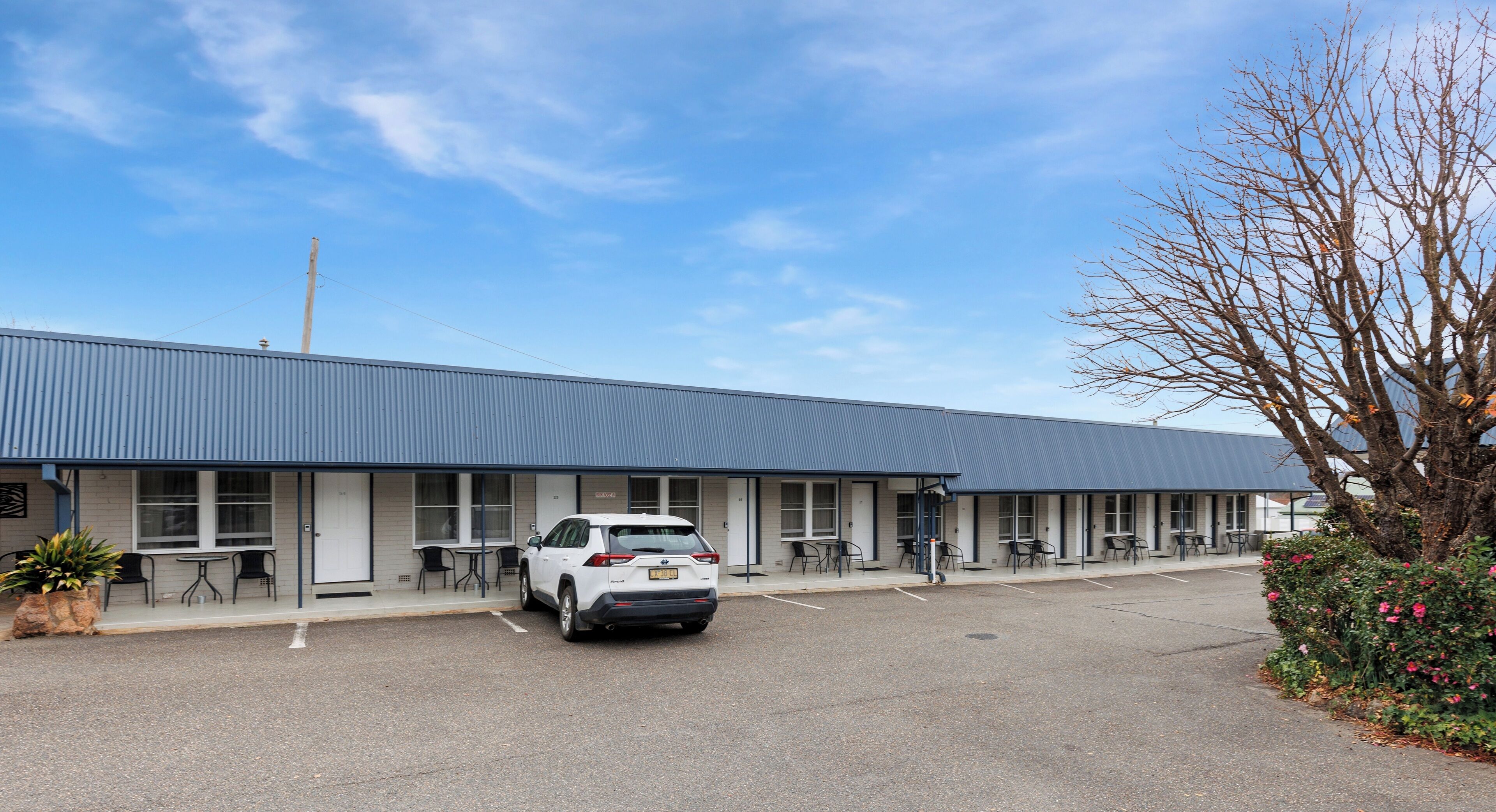 Un motel avec une rangée de chambres, un parking et un VUS blanc garé devant.