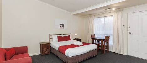 A hotel room with a bed, a red sofa, a wooden table, and a window with curtains.