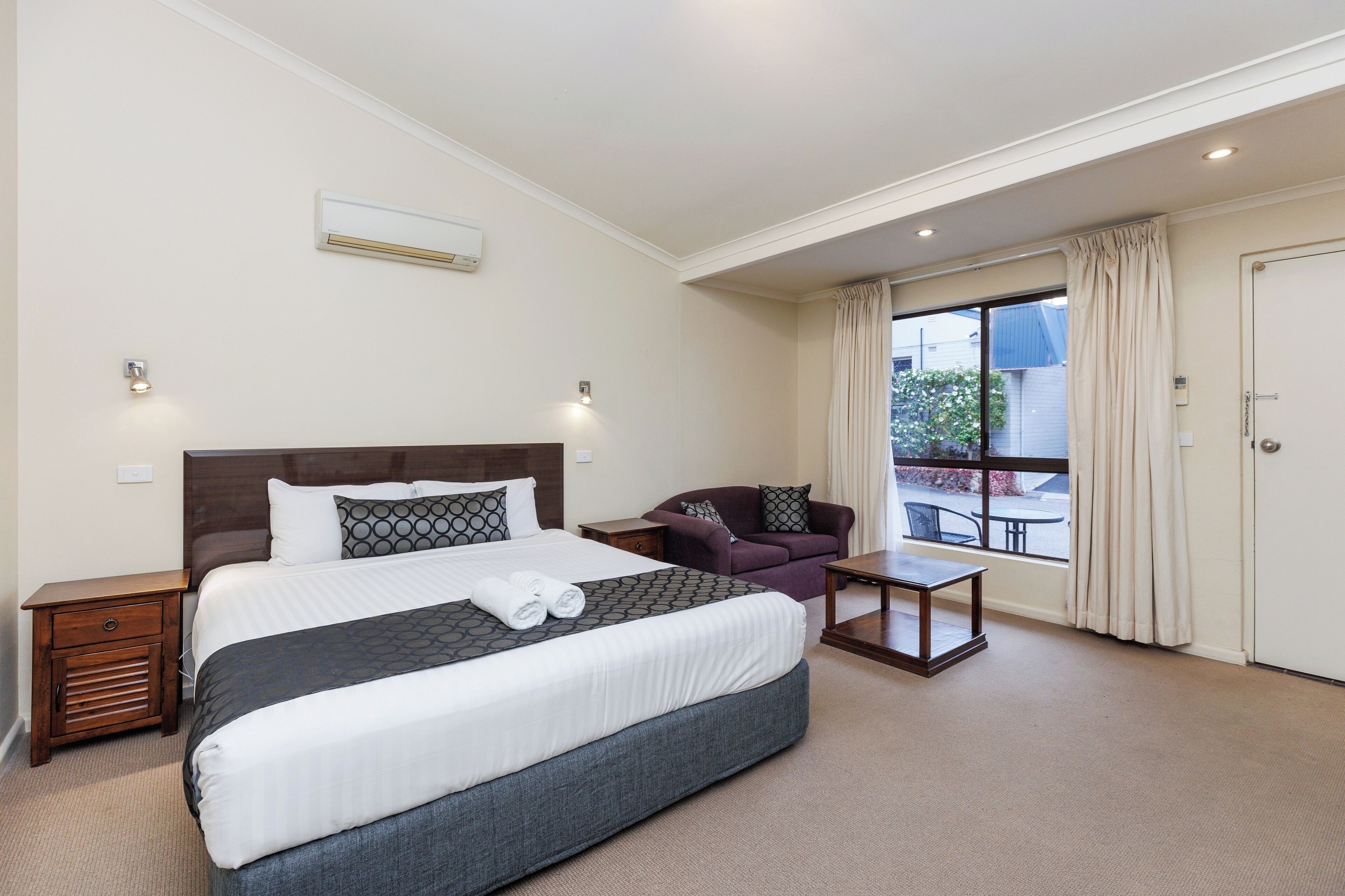 A hotel room with a large bed, a sofa, a small table, and a window with curtains.