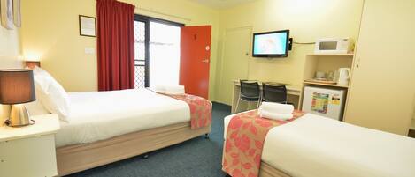A hotel room with two beds, a TV, a microwave, and a small desk with a lamp.