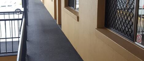 A corridor with a black carpet, beige walls, and windows with metal grilles.