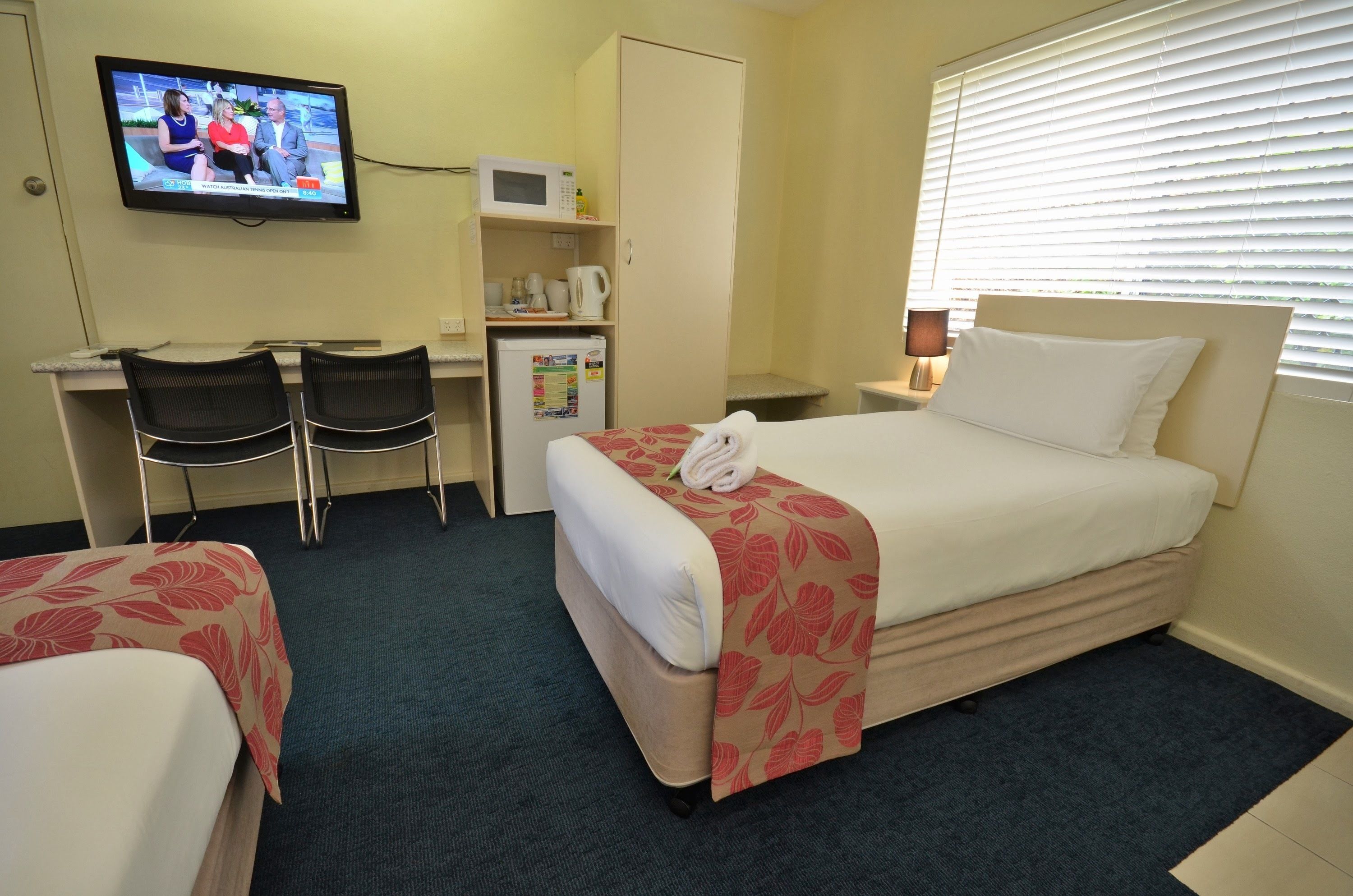 A hotel room with a bed, a desk with two chairs, a television, a microwave, and a refrigerator.