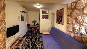 A cozy living area with a stone accent wall, a flat-screen TV, a patterned rug, a purple sofa, and a dining table with chairs. - Vila Vala (Dubrovnik)