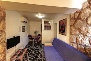 A cozy living area with a stone accent wall, a flat-screen TV, a patterned rug, a purple sofa, and a dining table with chairs.