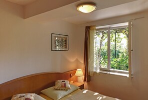 Habitación de hotel con una cama, una mesita de noche con lámpara, una ventana con cortinas y un cuadro en la pared.