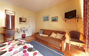 Una sala de estar acogedora con un sofá, sillas, un televisor, un lavamanos y un espejo.