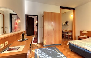 A hotel room with a wooden desk, a bed, a wardrobe, and a bathroom visible through an open door.