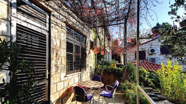 A courtyard with a table and chairs, a staircase, and a stone wall. - Vila Vala (Dubrovnik)