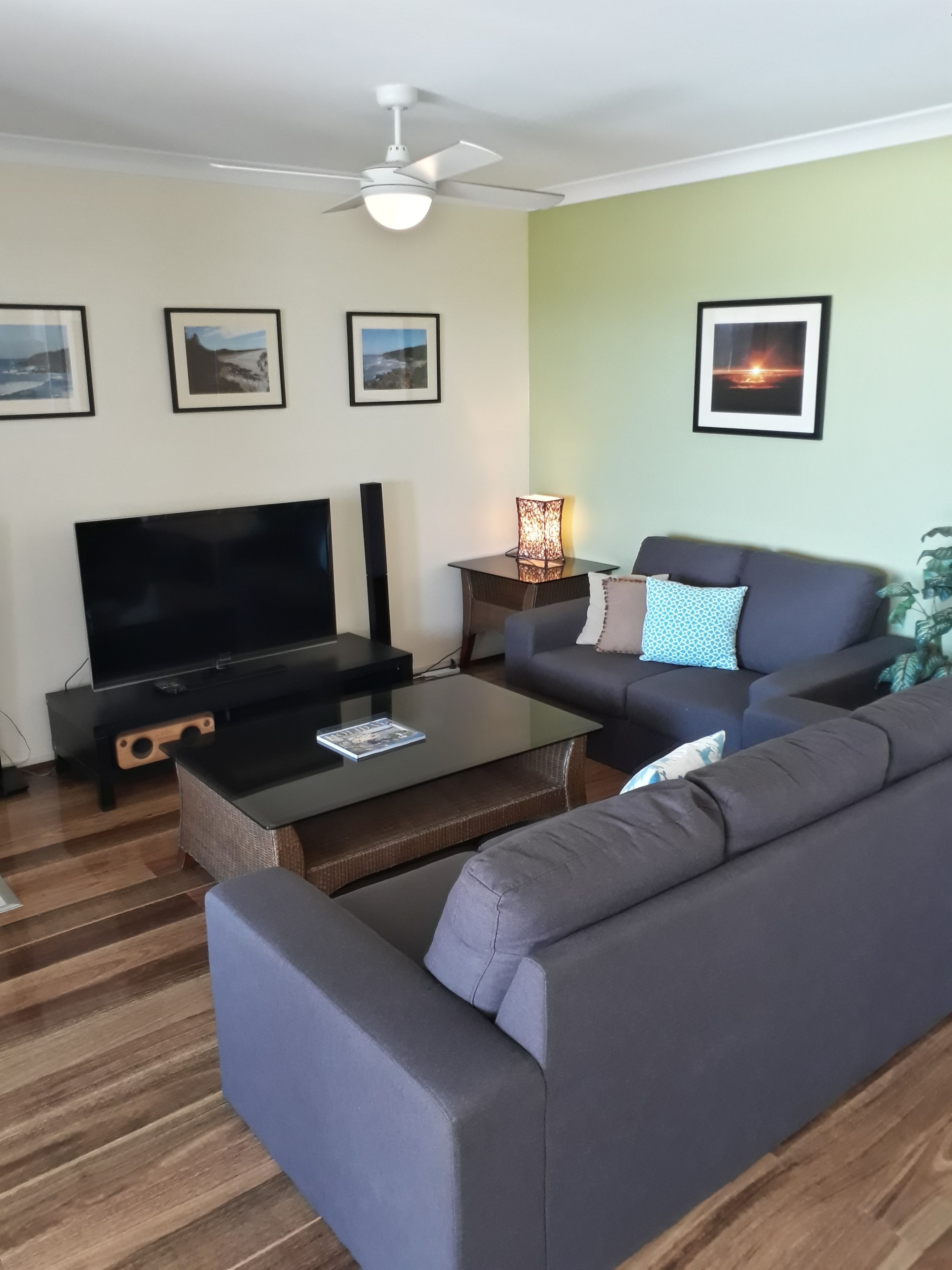 Ein Wohnzimmer mit Flachbildfernseher, einer Couch, einem Couchtisch und einem Deckenventilator.