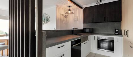 A modern kitchen with dark cabinetry, a built-in oven, and a large window.