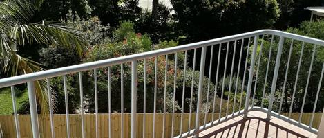 A balcony with a white railing, a small white table, and a view of a residential area with trees and houses.