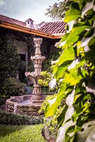 Una fuente de piedra de varios niveles, rodeada de exuberante vegetación y un edificio con tejado de azulejos al fondo.
