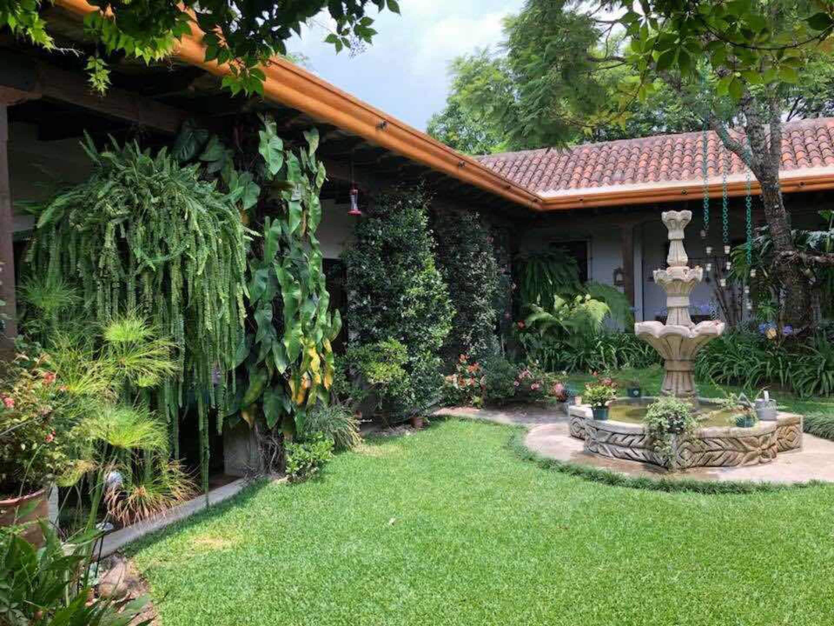 A well-maintained garden with a fountain, lush greenery, and a tiled roof.