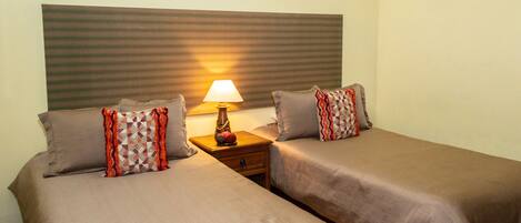 A double room with two beds, a nightstand with a lamp, and a decorative wall piece.