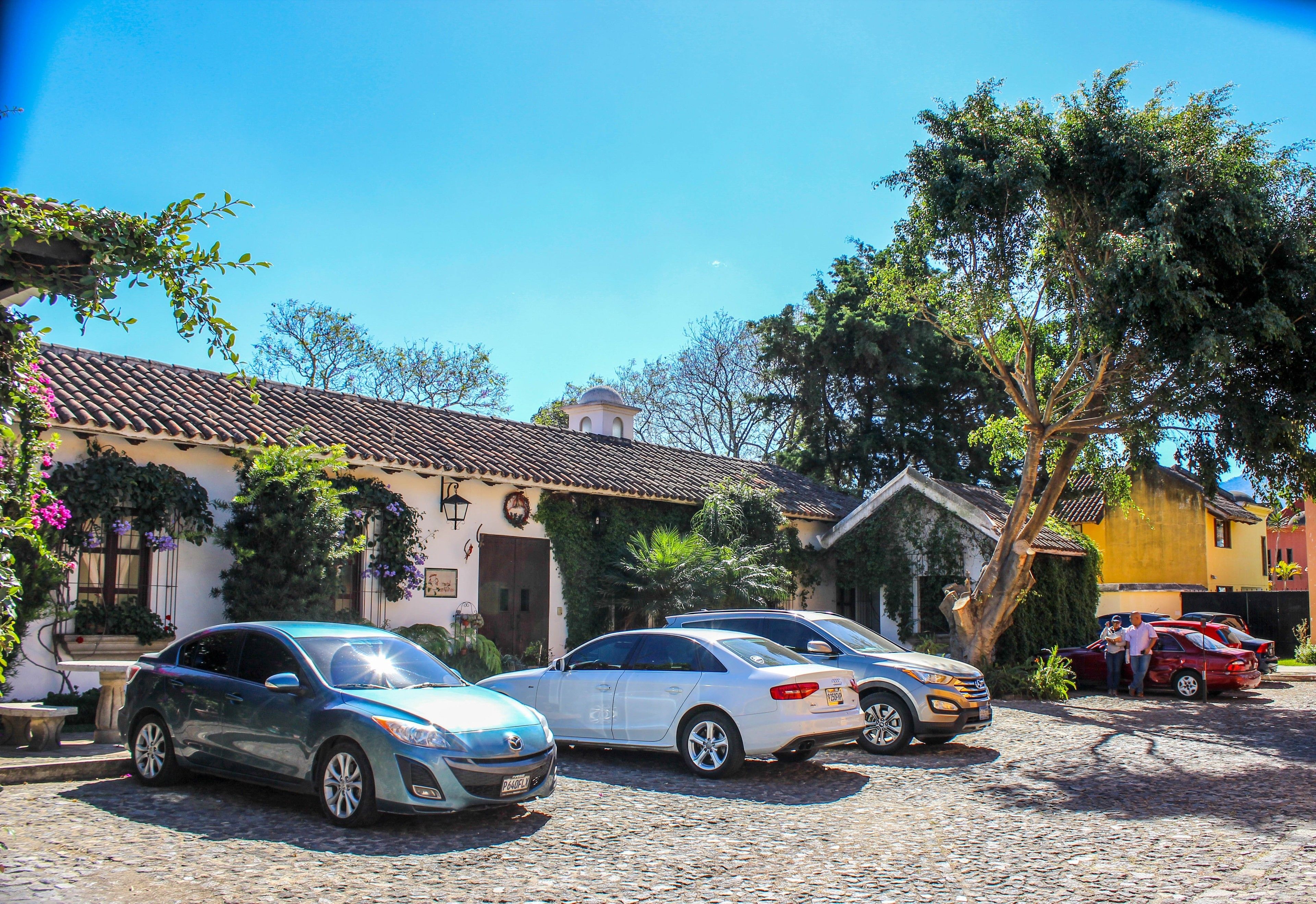 A cobblestone street with parked cars and a building with a tiled roof.