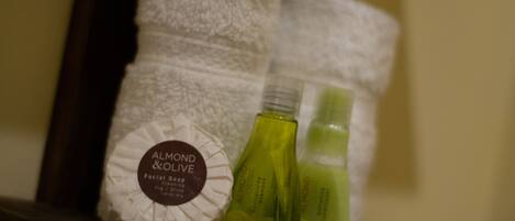 Een badkamerplank met een witte handdoek, amandelolie en een fles lotion.