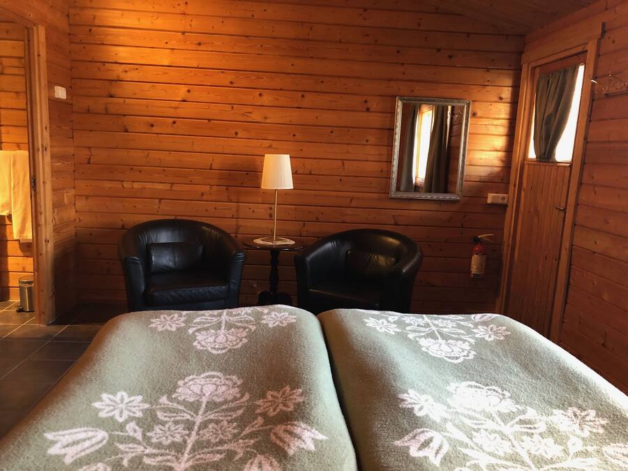A wooden cabin room with two leather chairs, a small table, a lamp, and a mirror on the wall.