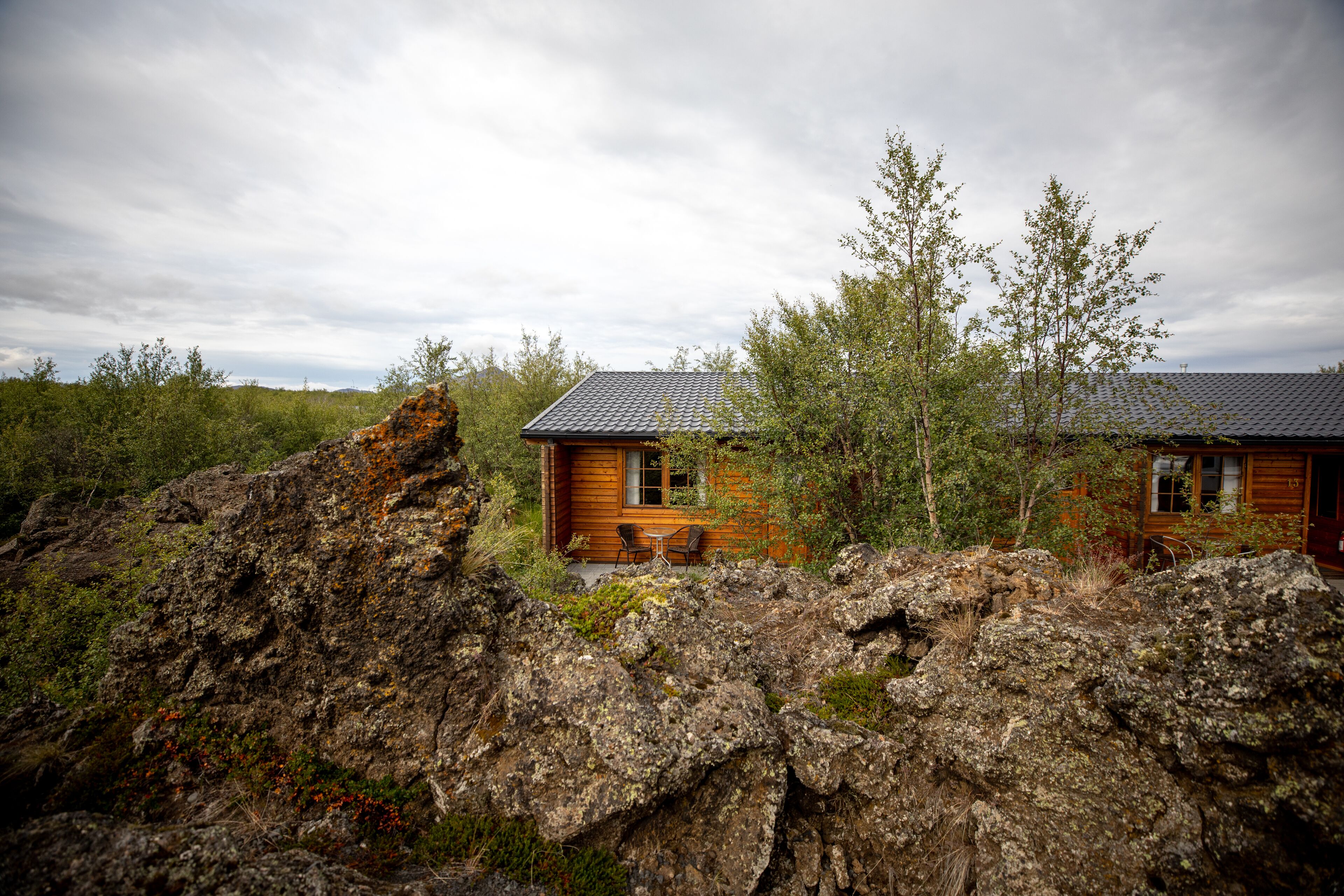 A wooden cabin with a tiled roof, surrounded by rocky terrain and sparse vegetation.